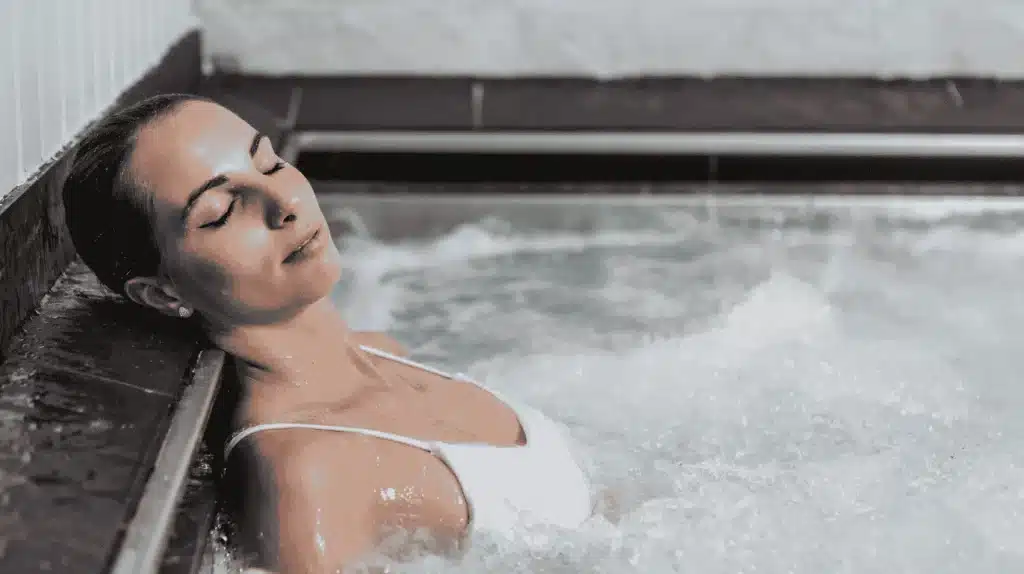 Femme se relaxant dans le jacuzzi d'un spa les yeux fermés, profitant d'une ambiance sonore et d'une atmosphère apaisante pour une expérience client optimale.